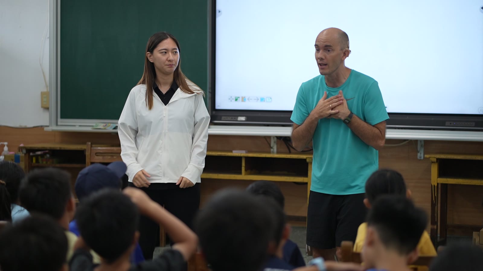 A teacher from overseas and a Taiwanese interpreter stand together in front of a class of children